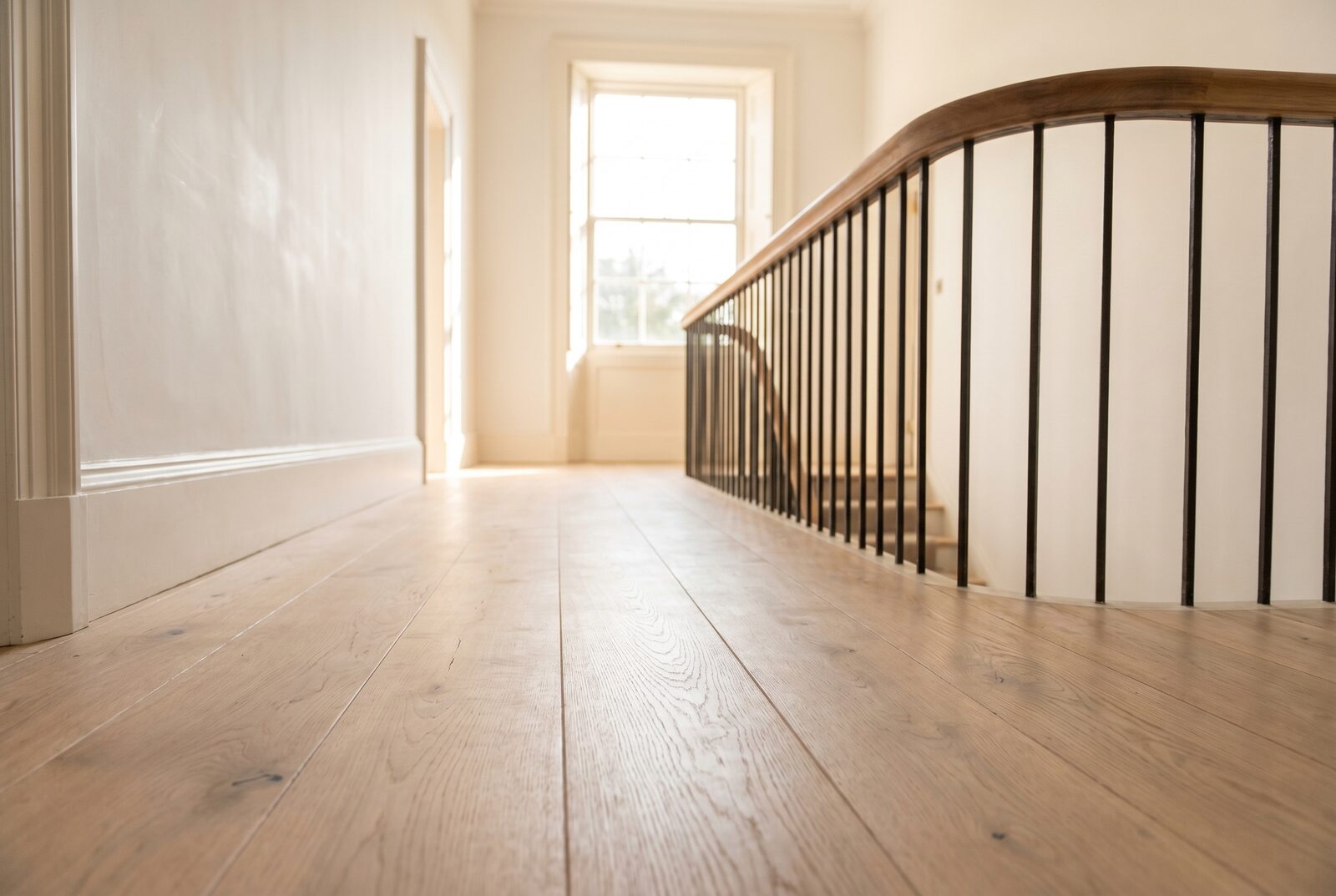 Pale limewashed European oak wide-plank running through a curved-balustrade hallway