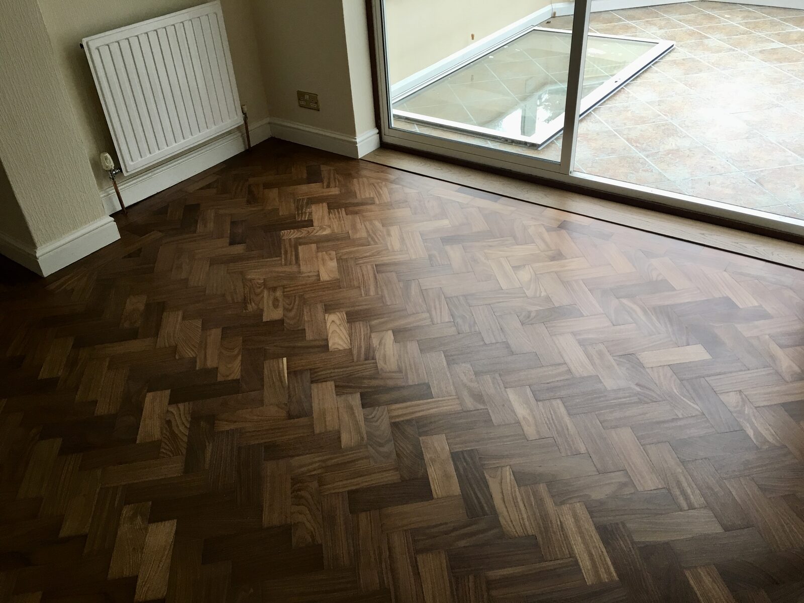 Glossy teak herringbone parquet floor in a room with patio doors