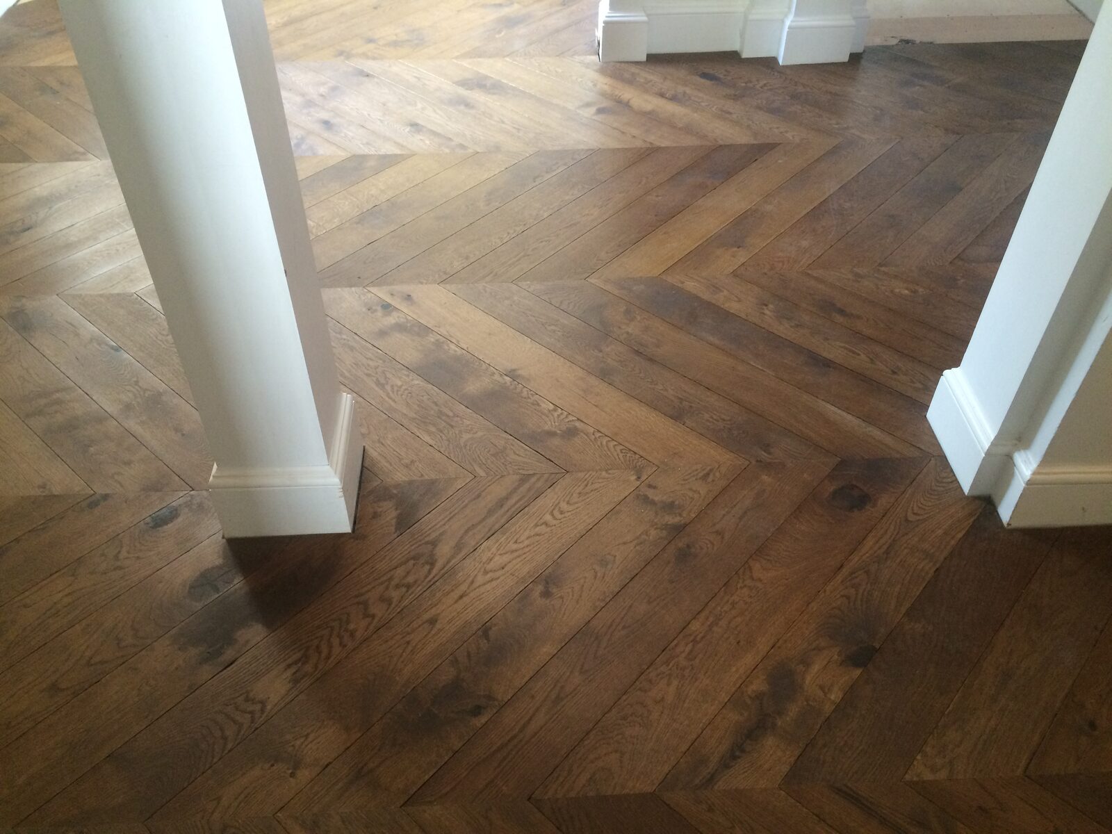 Warm oak chevron wood floor in a hallway beside white panelled doorways