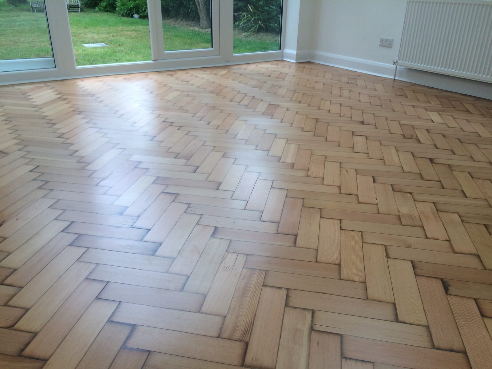 Warm amber reclaimed pine laid in a herringbone pattern in a sunlit garden room
