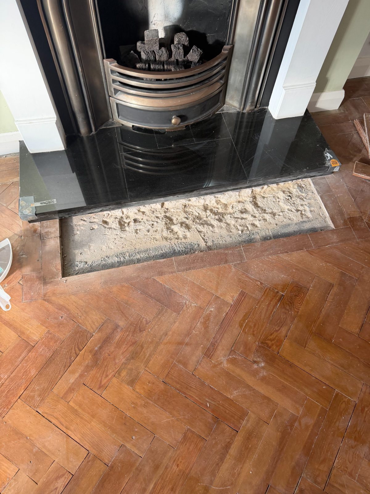 Aged pitch-pine herringbone parquet before restoration, with the granite fireplace hearth lifted to expose the subfloor