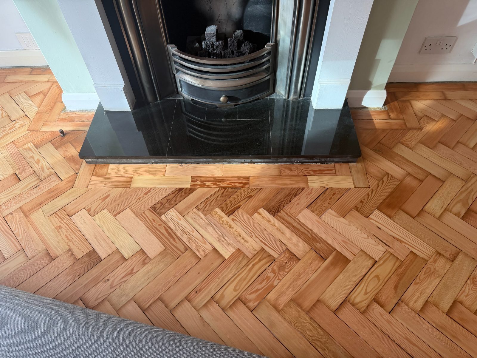 Restored pitch-pine herringbone parquet around a black granite fireplace hearth in an Elmer home