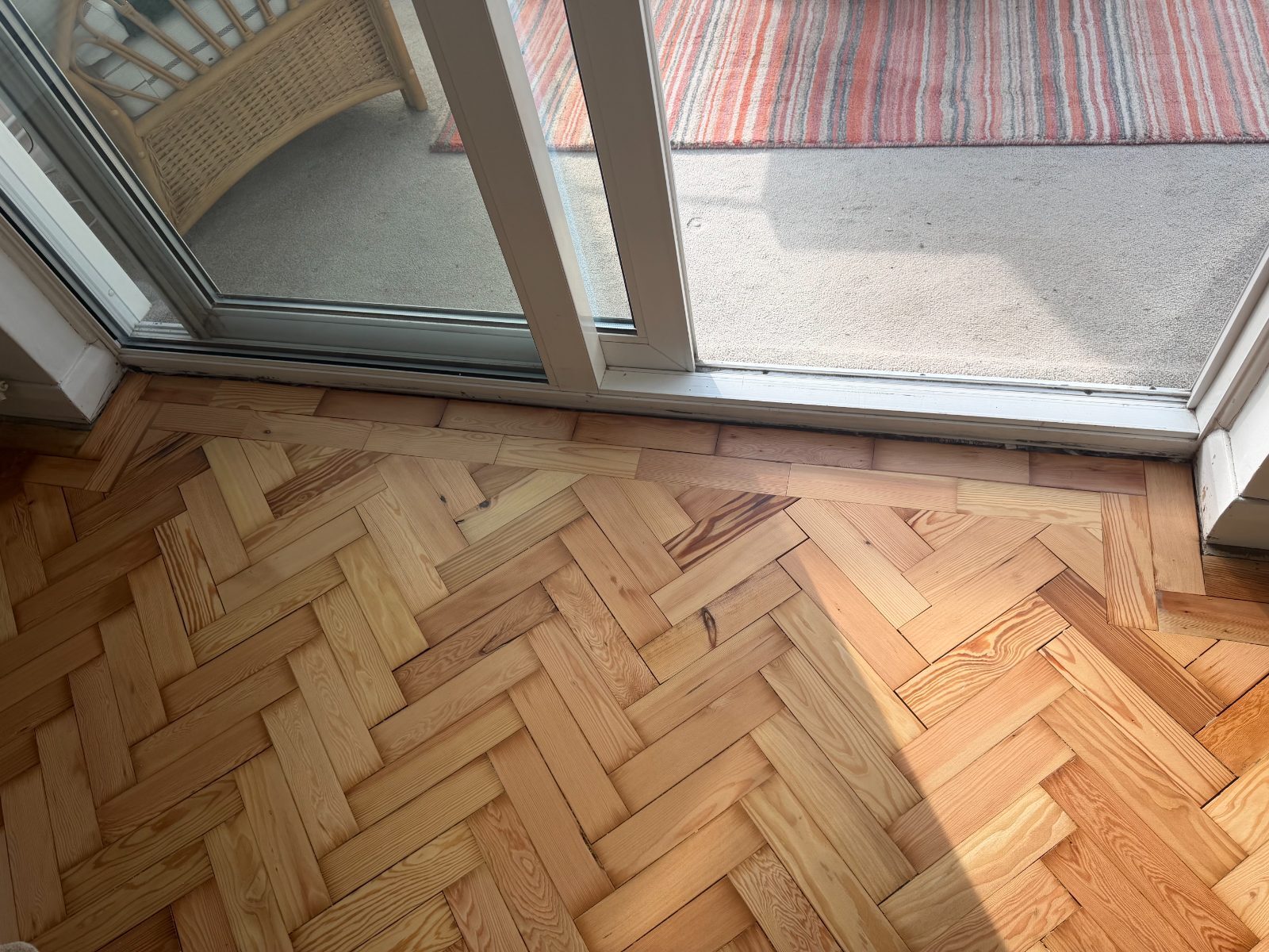 Freshly sanded pale-gold pitch-pine herringbone parquet at a sunlit patio door in an Elmer home