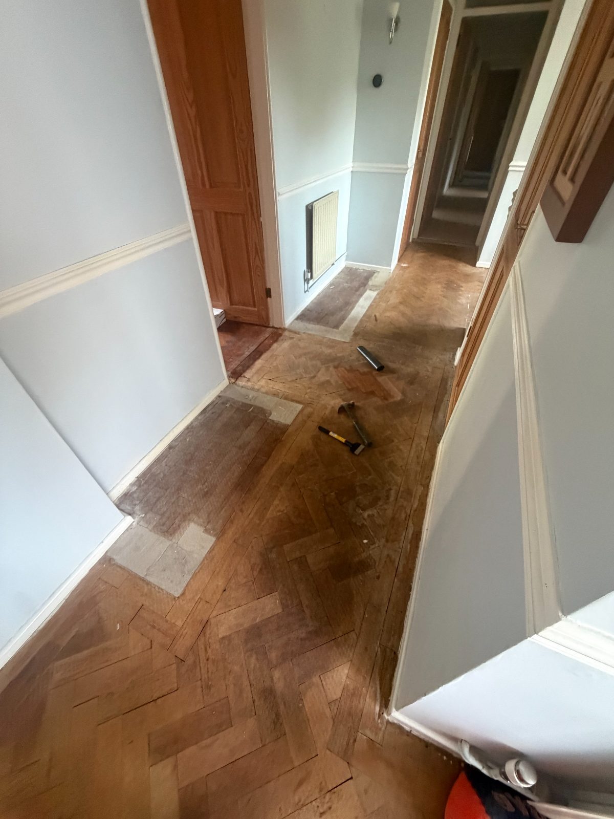 Reclaimed herringbone parquet lifted mid-restoration in a West Wittering hallway, hammer and chisel on the floor