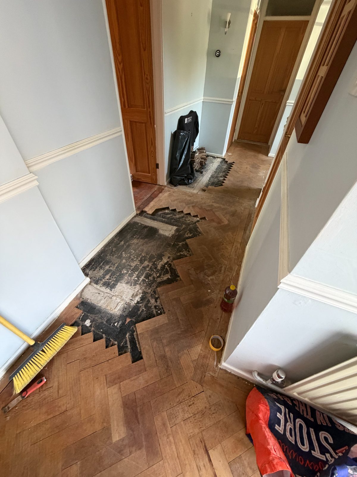 Herringbone parquet with sections lifted to the black bitumen subfloor, reclaimed blocks stacked ready to relay
