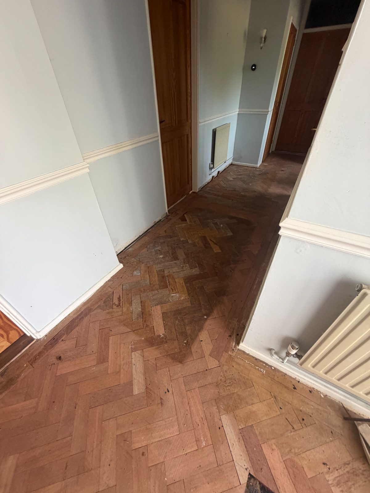 Repaired herringbone parquet with lighter reclaimed blocks patched into the older weave, not yet sanded
