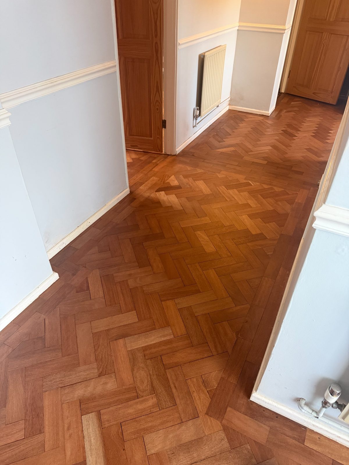 Finished reclaimed herringbone parquet, sanded and lacquered to a warm honey tone, running through into further rooms
