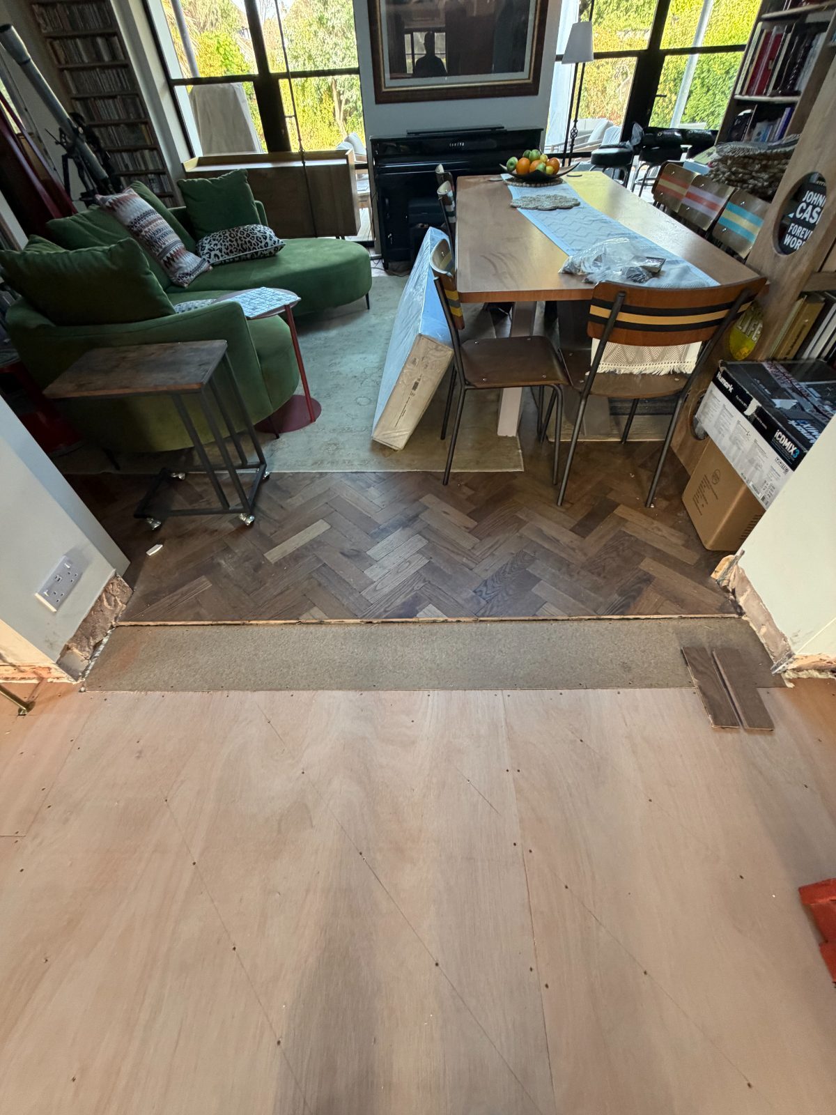 A prepared plywood subfloor in a Summerley Estate home, with the existing dark herringbone parquet beyond the threshold
