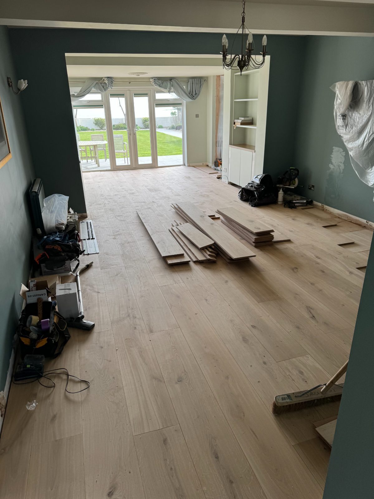 Pale unfinished engineered-oak boards part-laid over a new subfloor in an Elmer home, with stacked planks and a mitre saw during installation