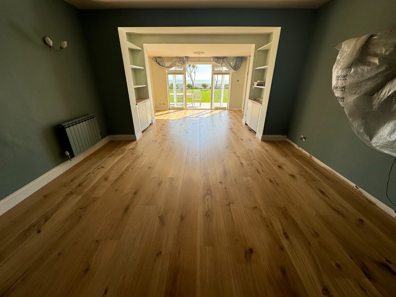 Warm honey engineered-oak plank flooring, freshly sanded and lacquered, running to sea-view French doors in a detached Elmer home