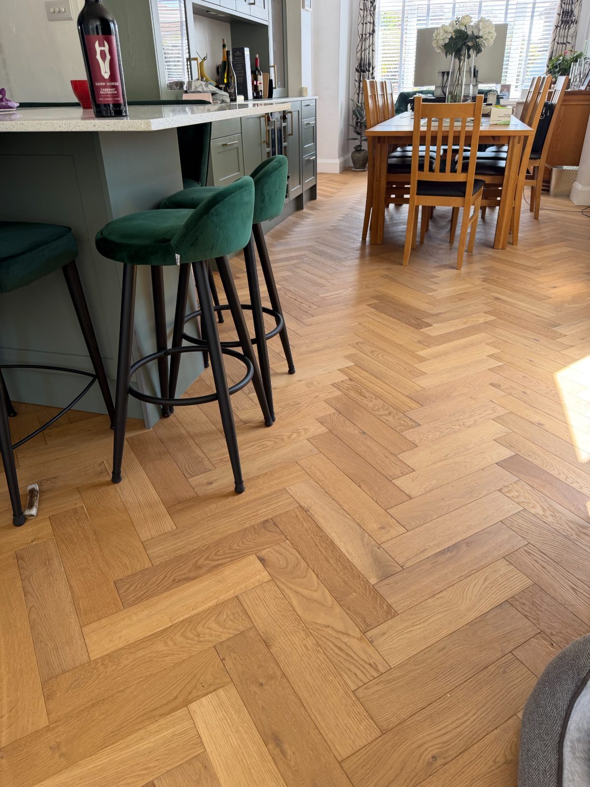 Warm honey oak herringbone parquet in a Felpham open-plan kitchen and dining room, laid past a green island out to the dining table