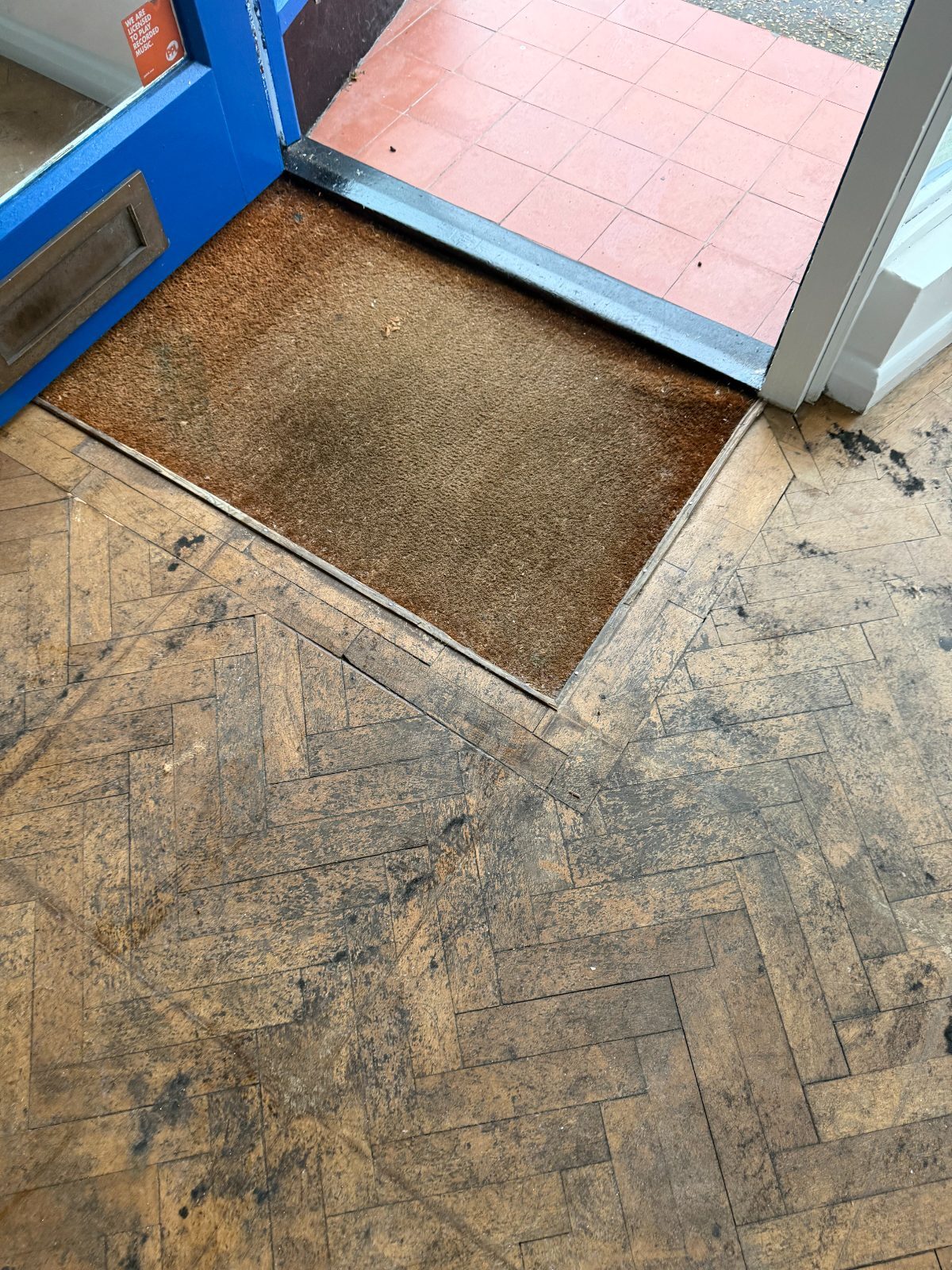 A worn, blackened old herringbone block floor at a Felpham shop doorway, before restoration