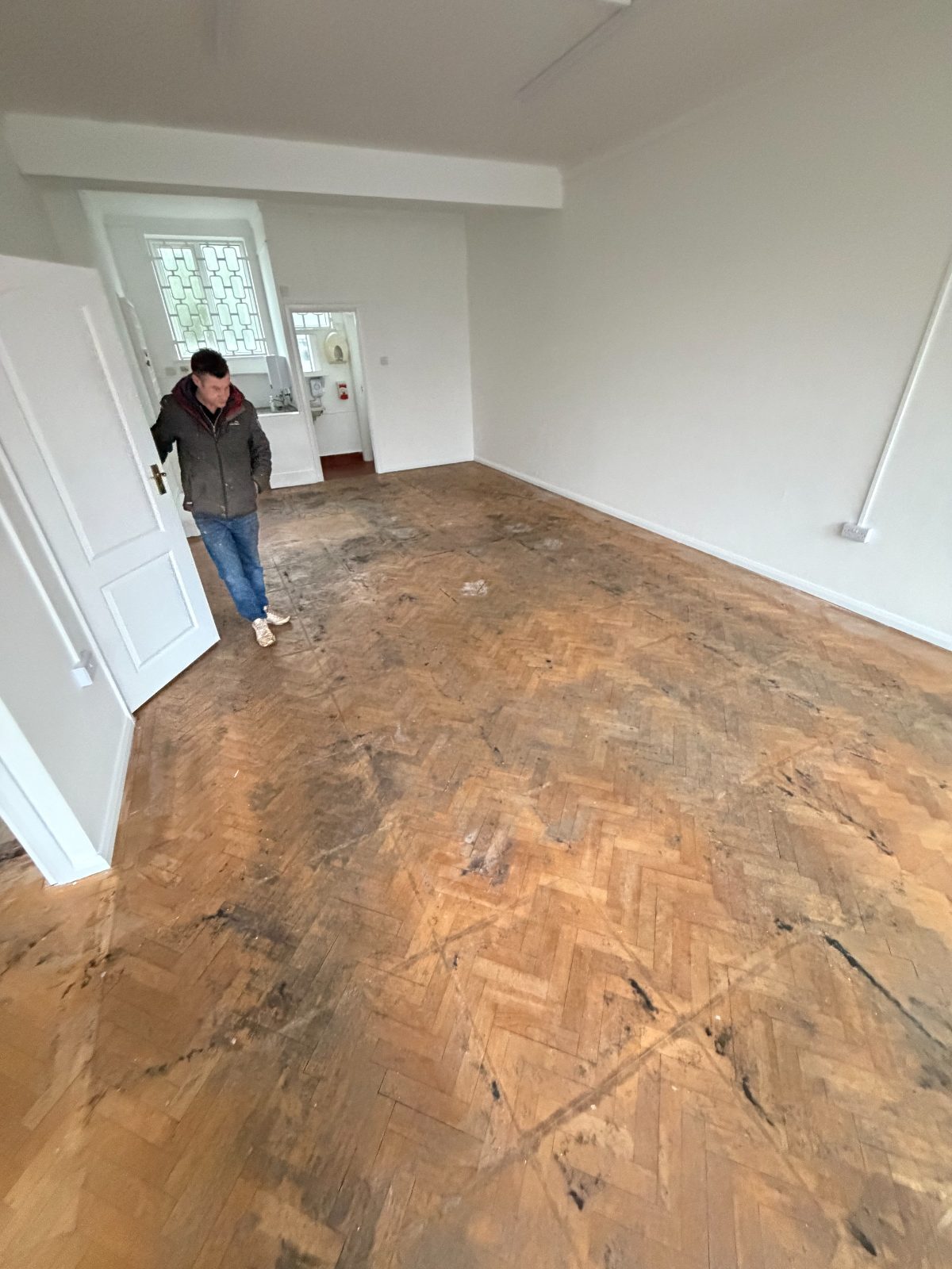 An original herringbone block floor uncovered in an empty Felpham room, still blackened with old bitumen staining before restoration