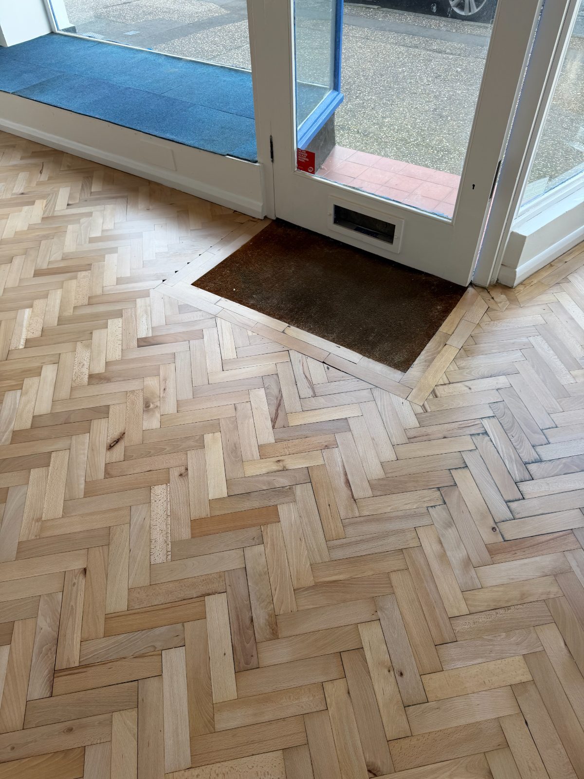 Freshly restored pale herringbone parquet running up to the glazed double doors of a Felpham shop