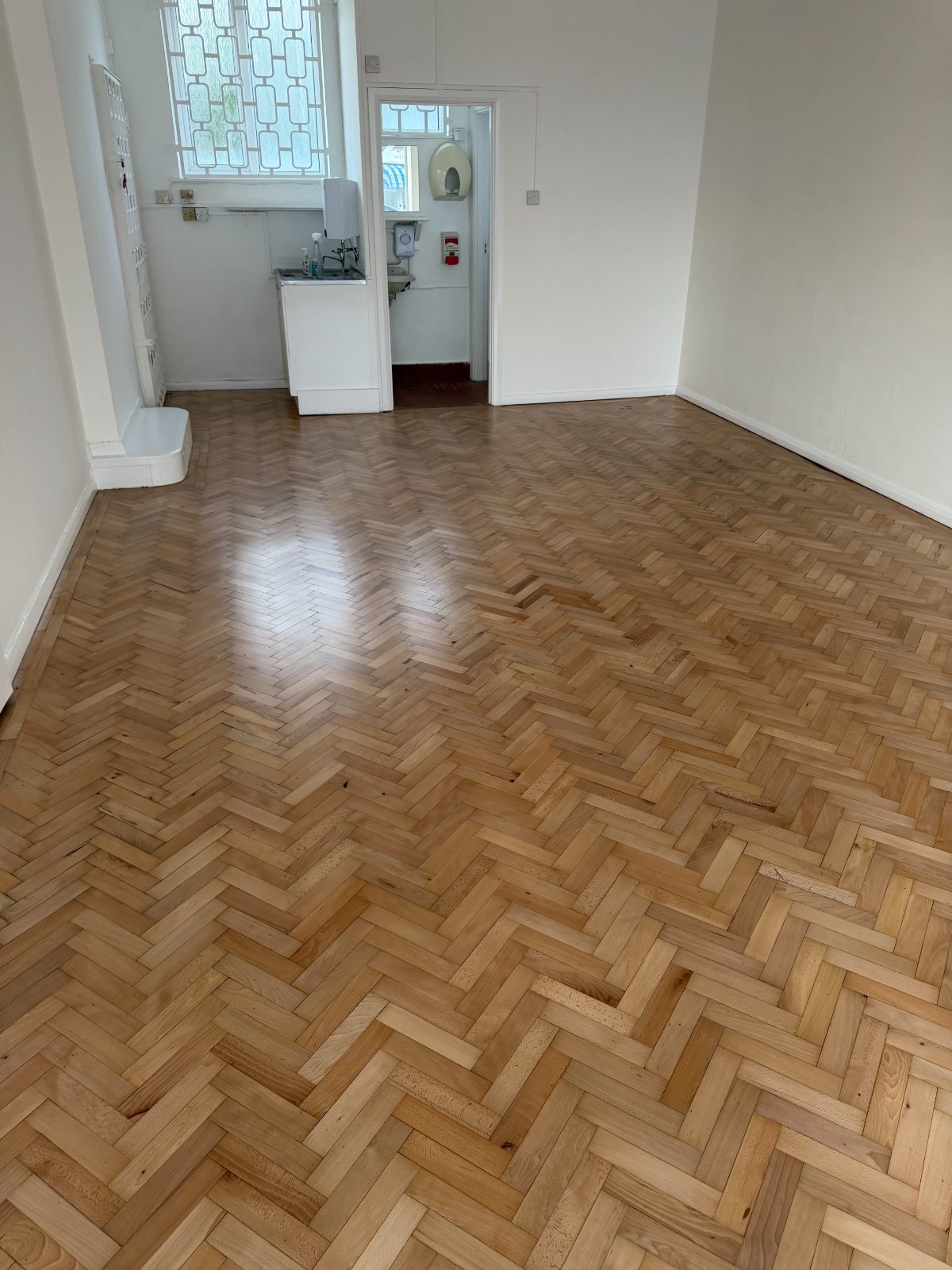 A restored pale herringbone parquet floor sanded back to a clean, even finish in a bright Felpham shop