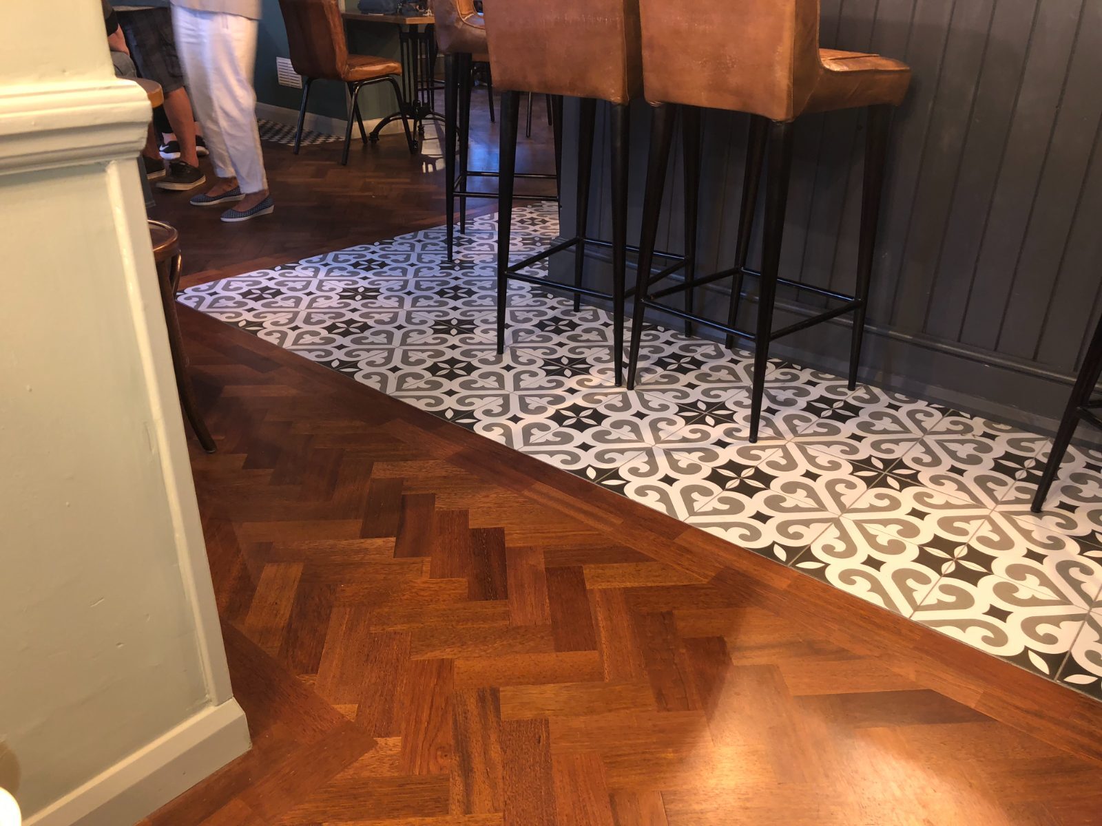 Rich dark-toned herringbone parquet laid in a Felpham pub bar, run up to a band of patterned feature tiles