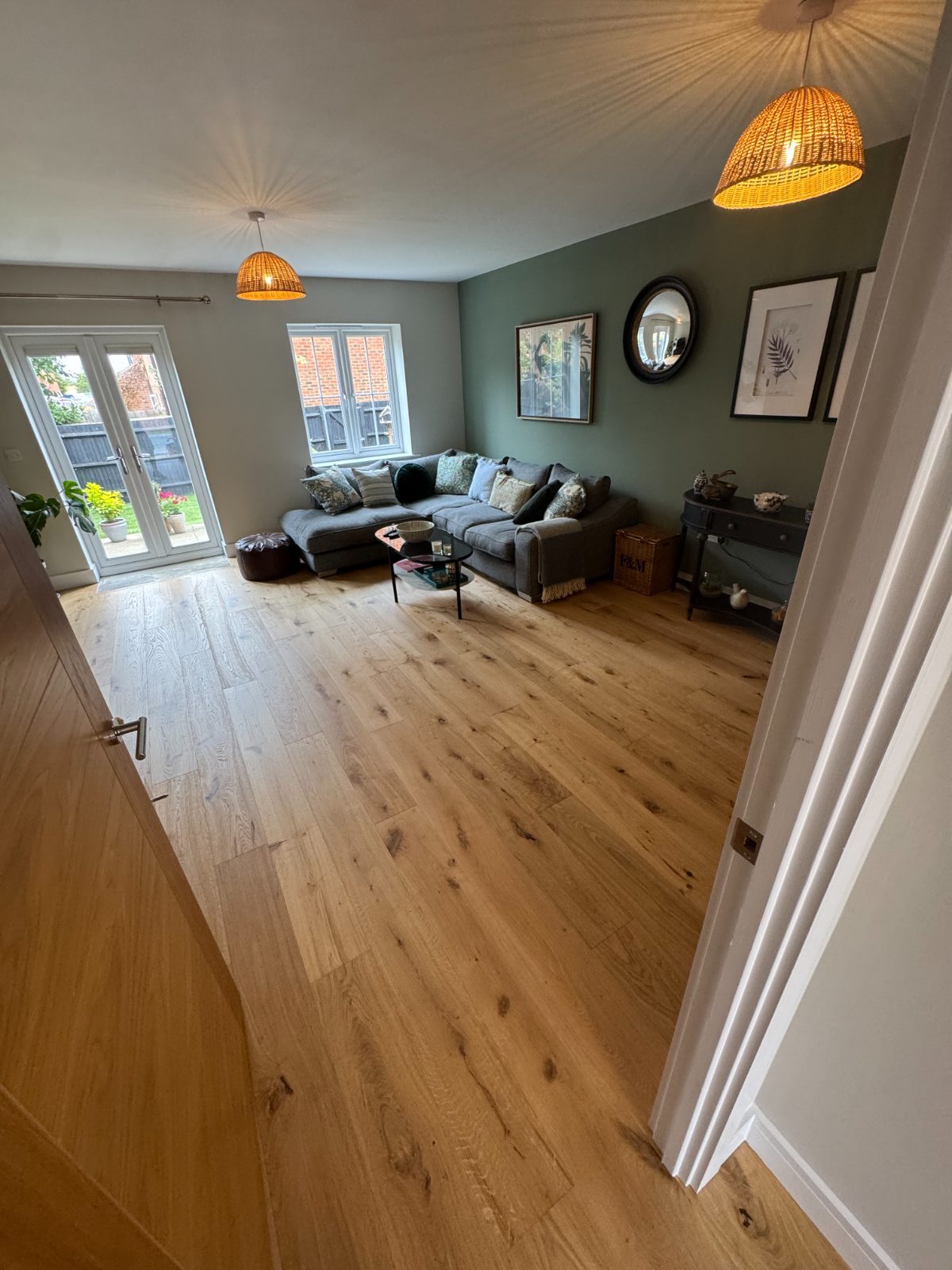 Honey-toned character oak engineered flooring in an open-plan Bognor Regis living room with a sage-green wall and french doors to the garden