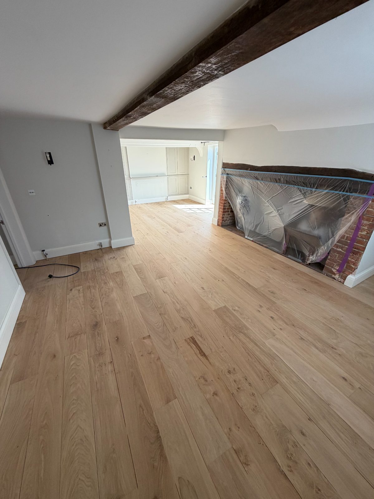 Solid oak wide-plank flooring sanded to bare natural timber ready for staining in a beamed Slindon period living room, chimney breast sheeted for dust protection