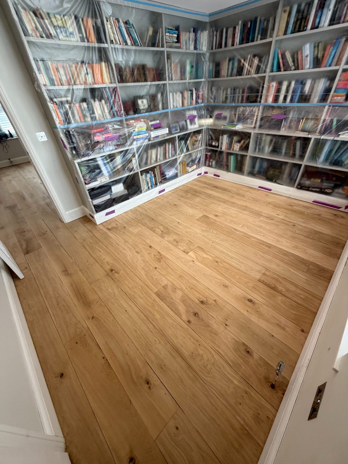 Solid oak wide-plank flooring sanded to bare natural timber before staining in a Slindon period library, fitted bookcases sheeted in plastic for dust protection
