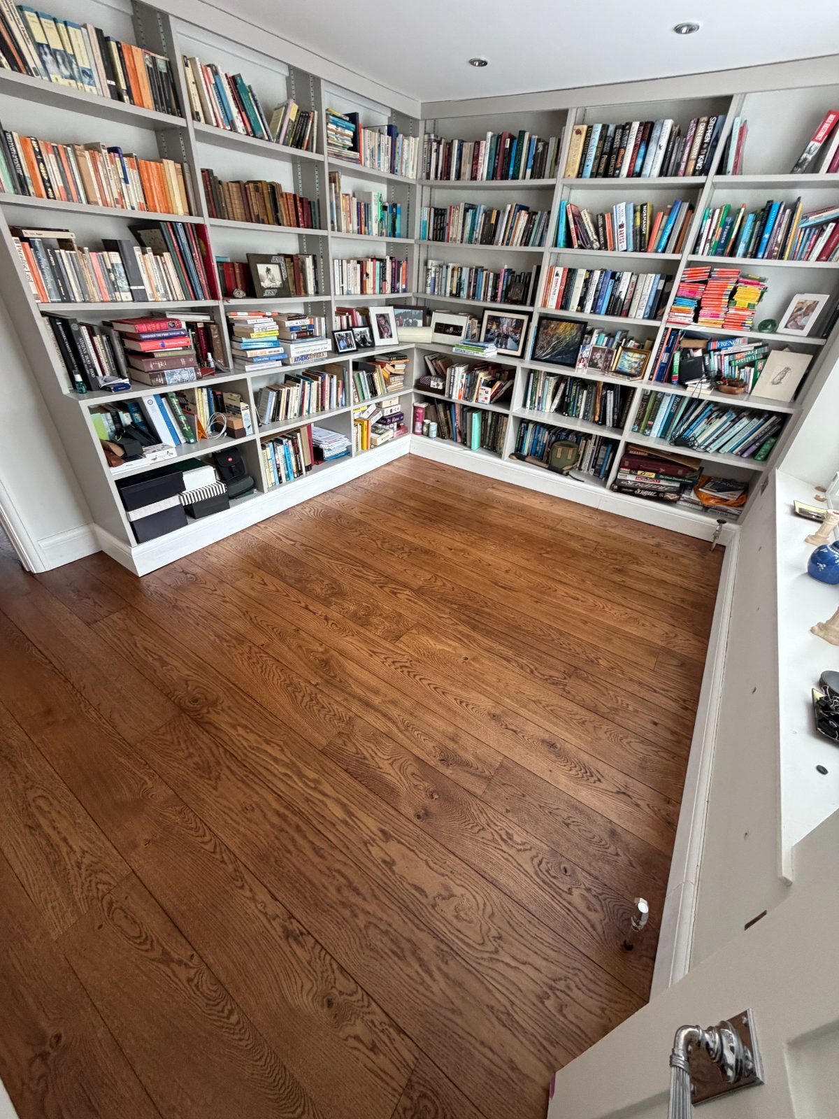 Restored solid oak wide-plank flooring finished in a warm walnut stain and matt hard-wax oil in a period library lined with full fitted bookcases, in a Slindon cottage