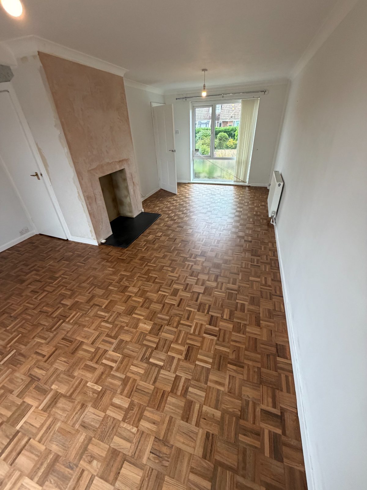 A restored mosaic-block parquet floor in a Westergate living room, sanded back and refinished to a natural warm oak in a low-sheen matt, with a freshly plastered chimney breast
