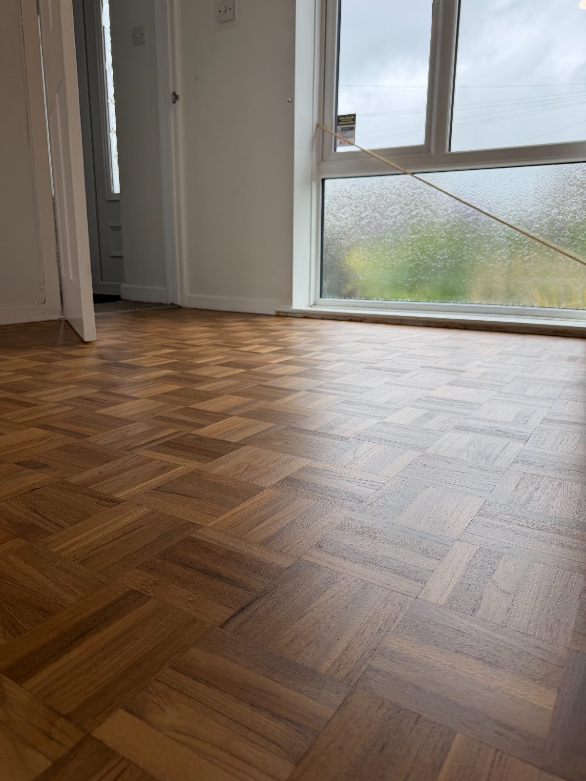 Restored mosaic-block parquet flooring in a bright Westergate reception room, refinished to a pale natural oak and catching the daylight from a tall window onto the garden, with an internal doorway to one side
