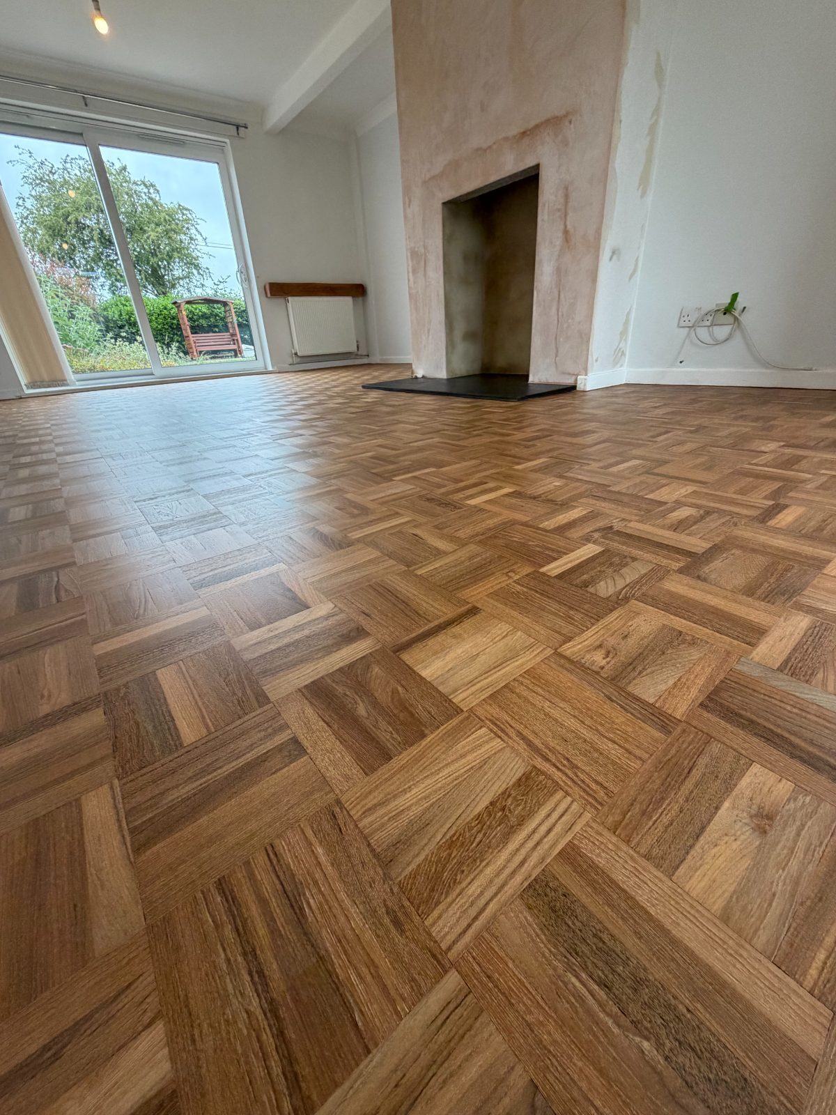 A restored mosaic-block parquet floor in a bright Westergate reception room, its little basket-weave squares refinished to a warm natural oak, with sliding doors onto the garden