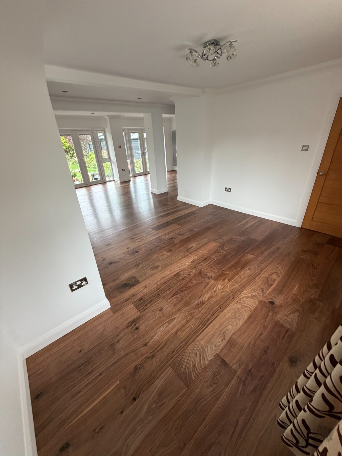 Restored wide-plank walnut flooring in a rich satin finish, running from a Felpham hallway through an open-plan room to French doors