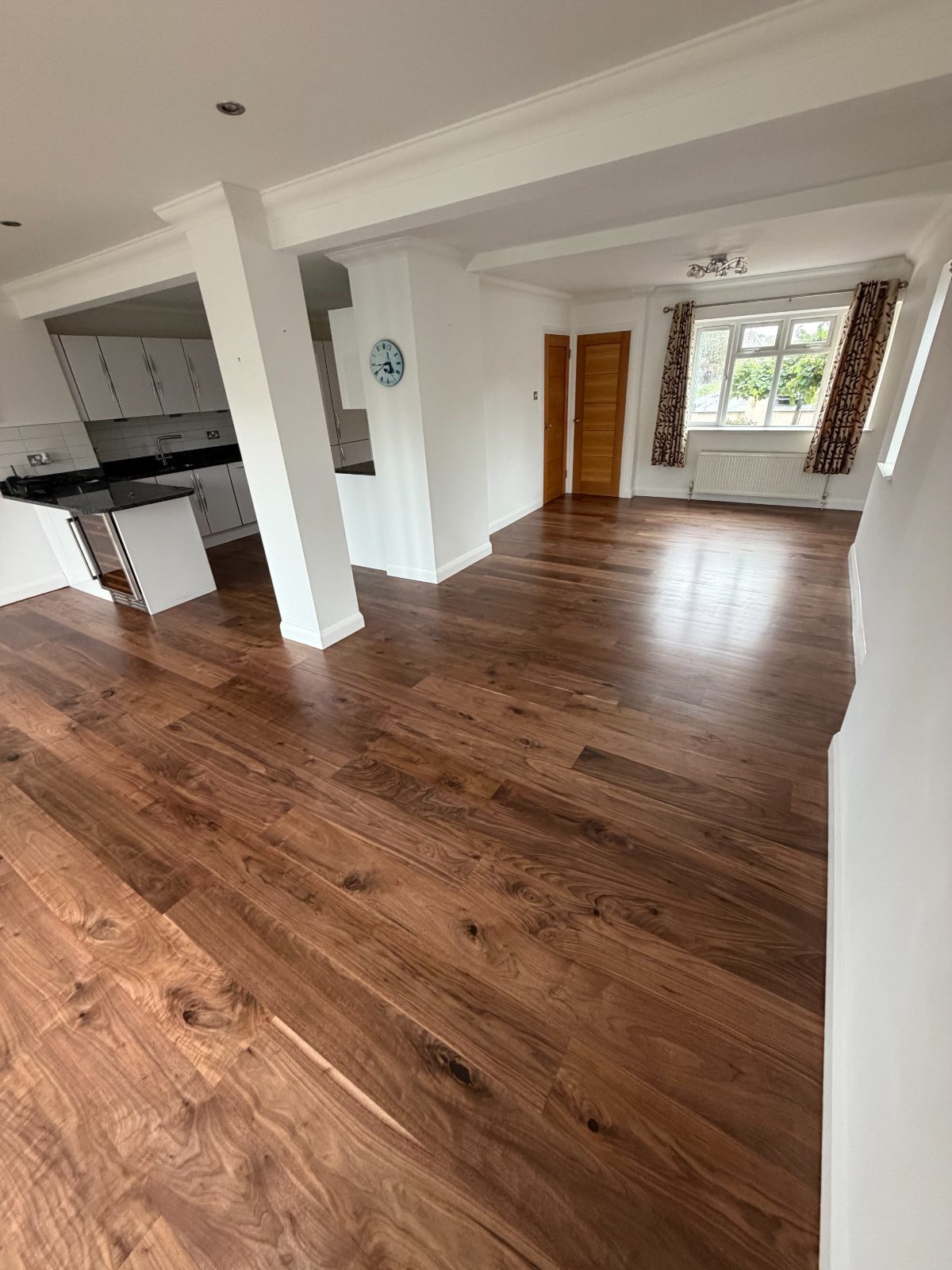 Restored wide-plank walnut flooring through a Felpham open-plan kitchen and dining room, running under square pillars to a bay window