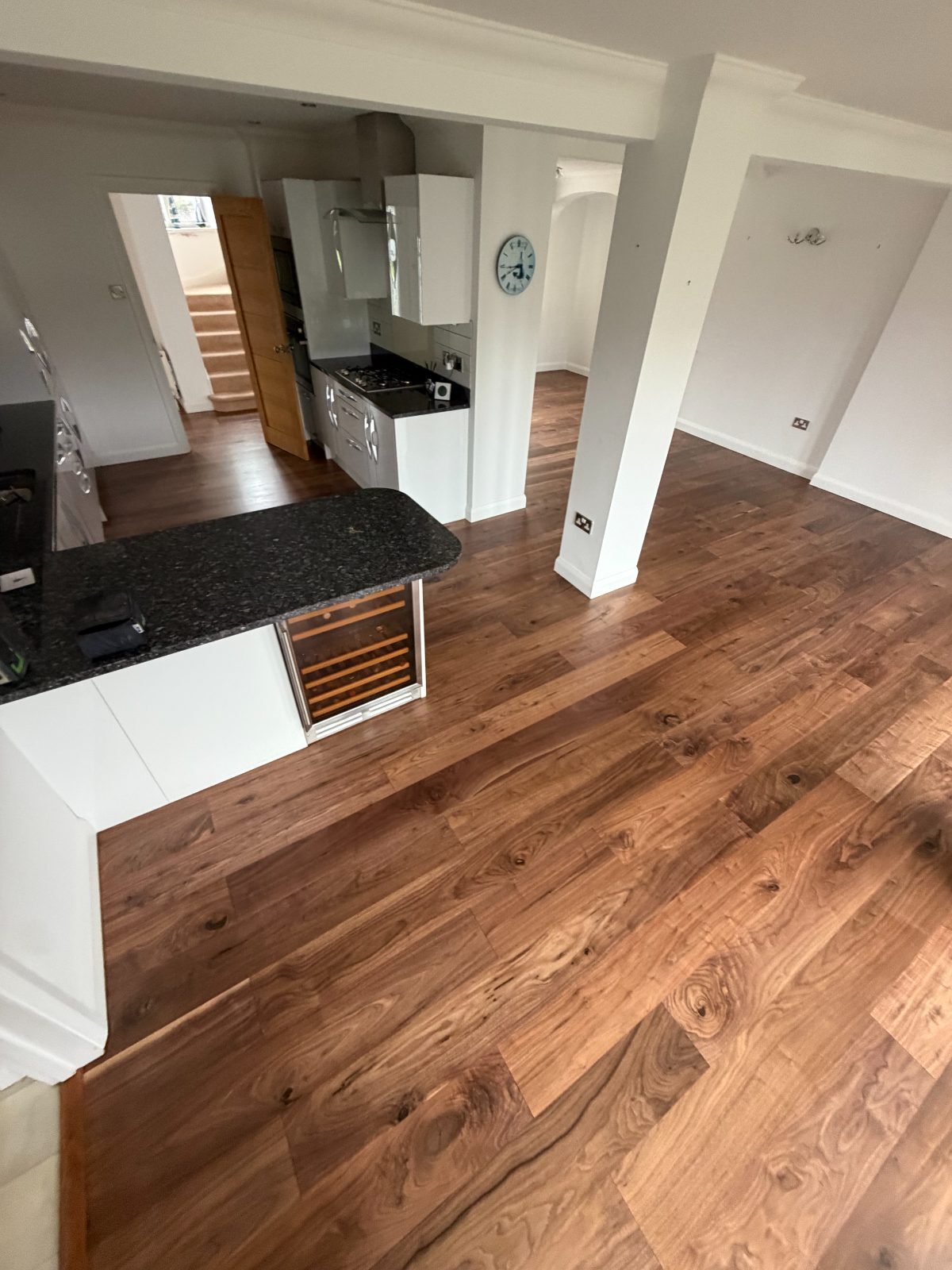 Refinished wide-plank walnut flooring running round a granite kitchen peninsula towards the hall and staircase of a Felpham detached house