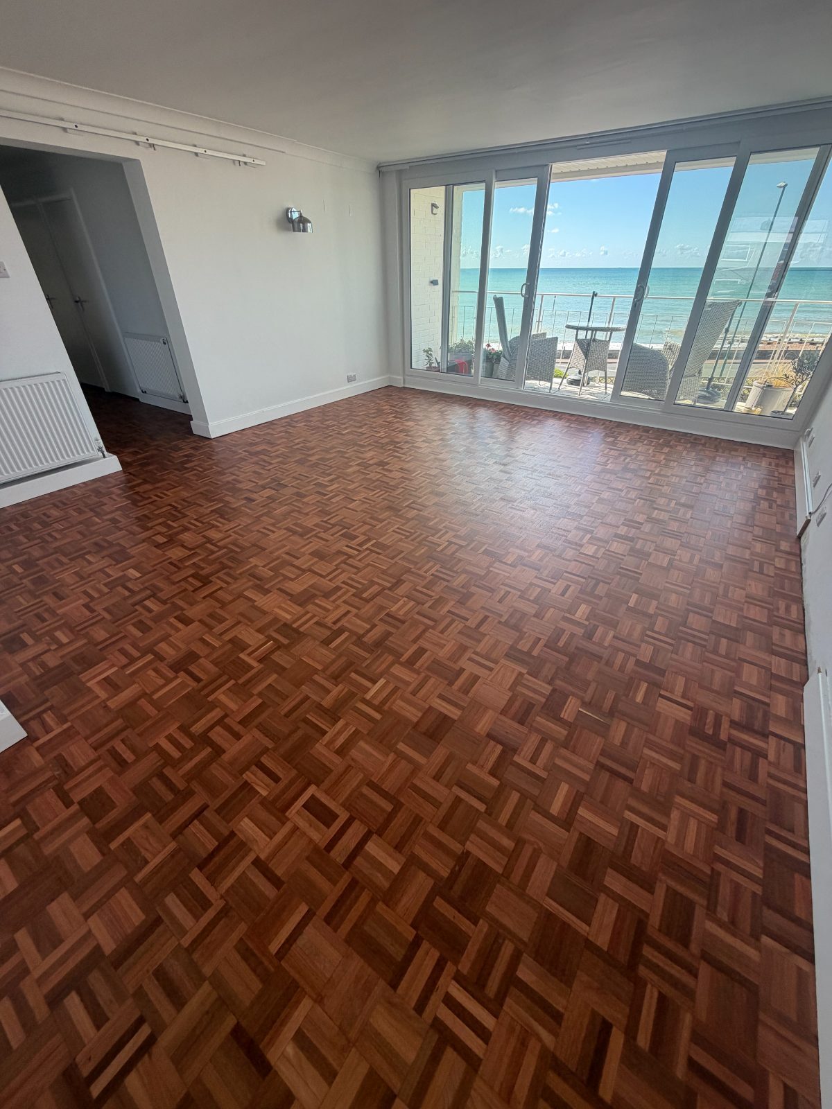 Restored mosaic parquet flooring with a fresh even sheen in a bright Rustington seafront lounge, the sea beyond the full-width sliding doors