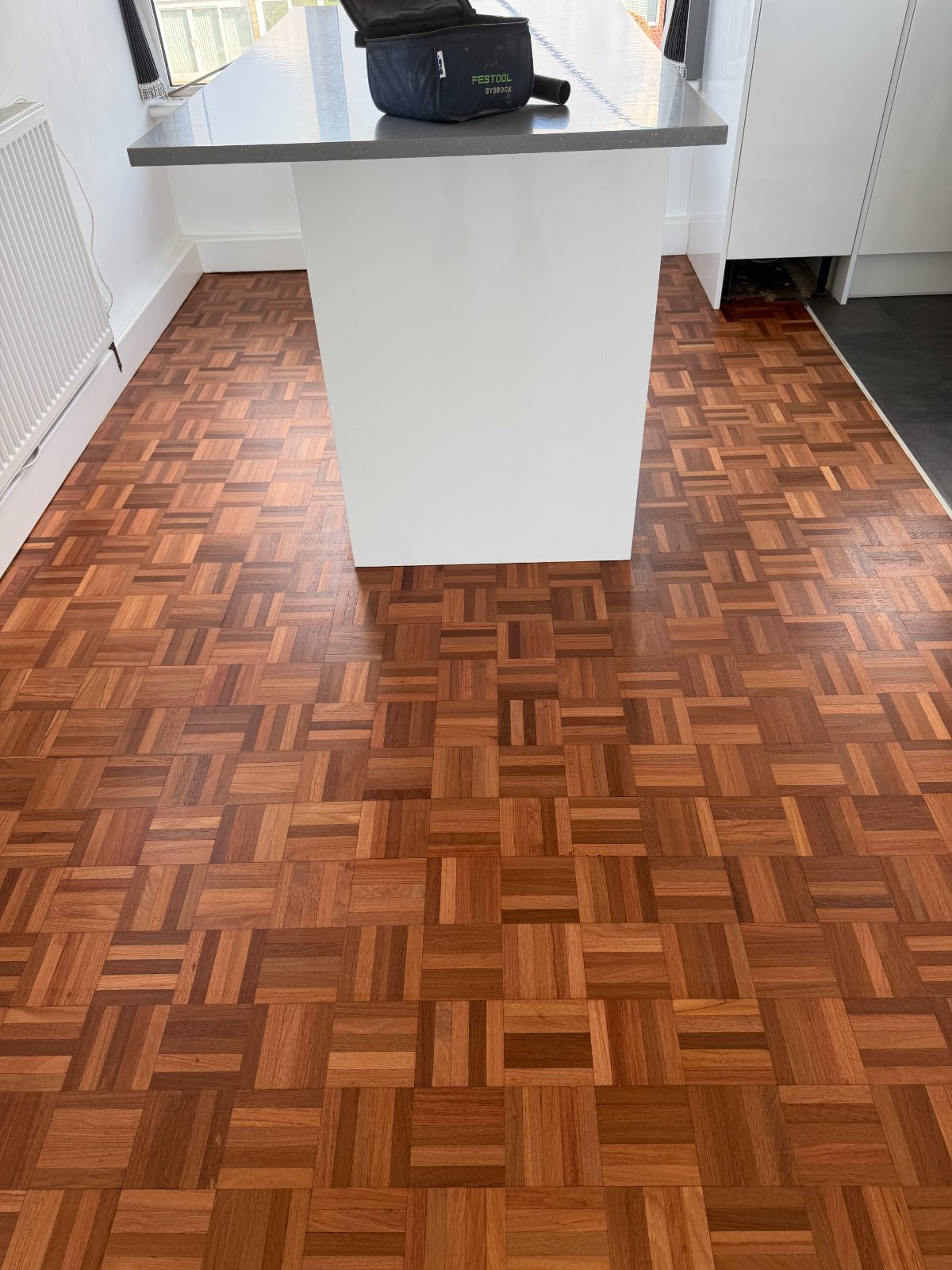 Refinished mosaic parquet in an even warm tone around a white kitchen island in a Rustington seafront flat