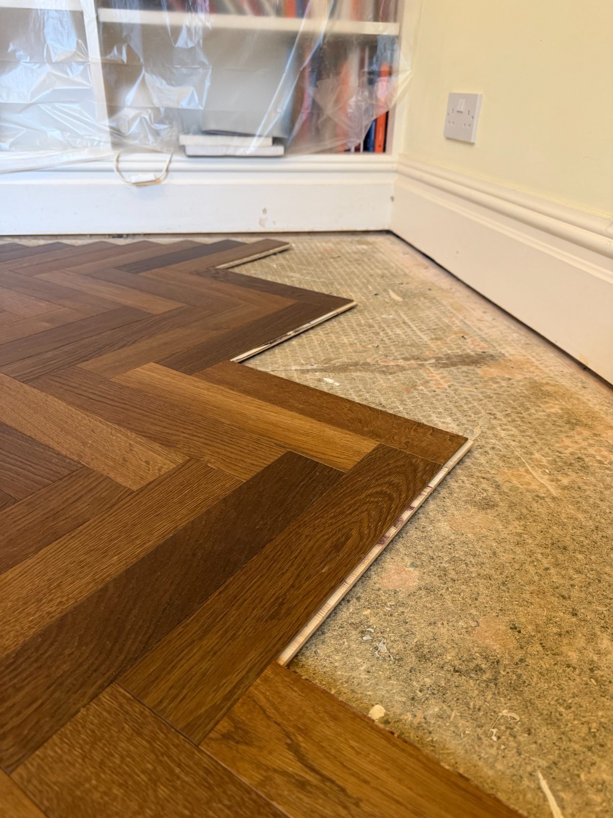 Oak herringbone parquet blocks being laid over a prepared subfloor beside a painted period skirting board at Burton House