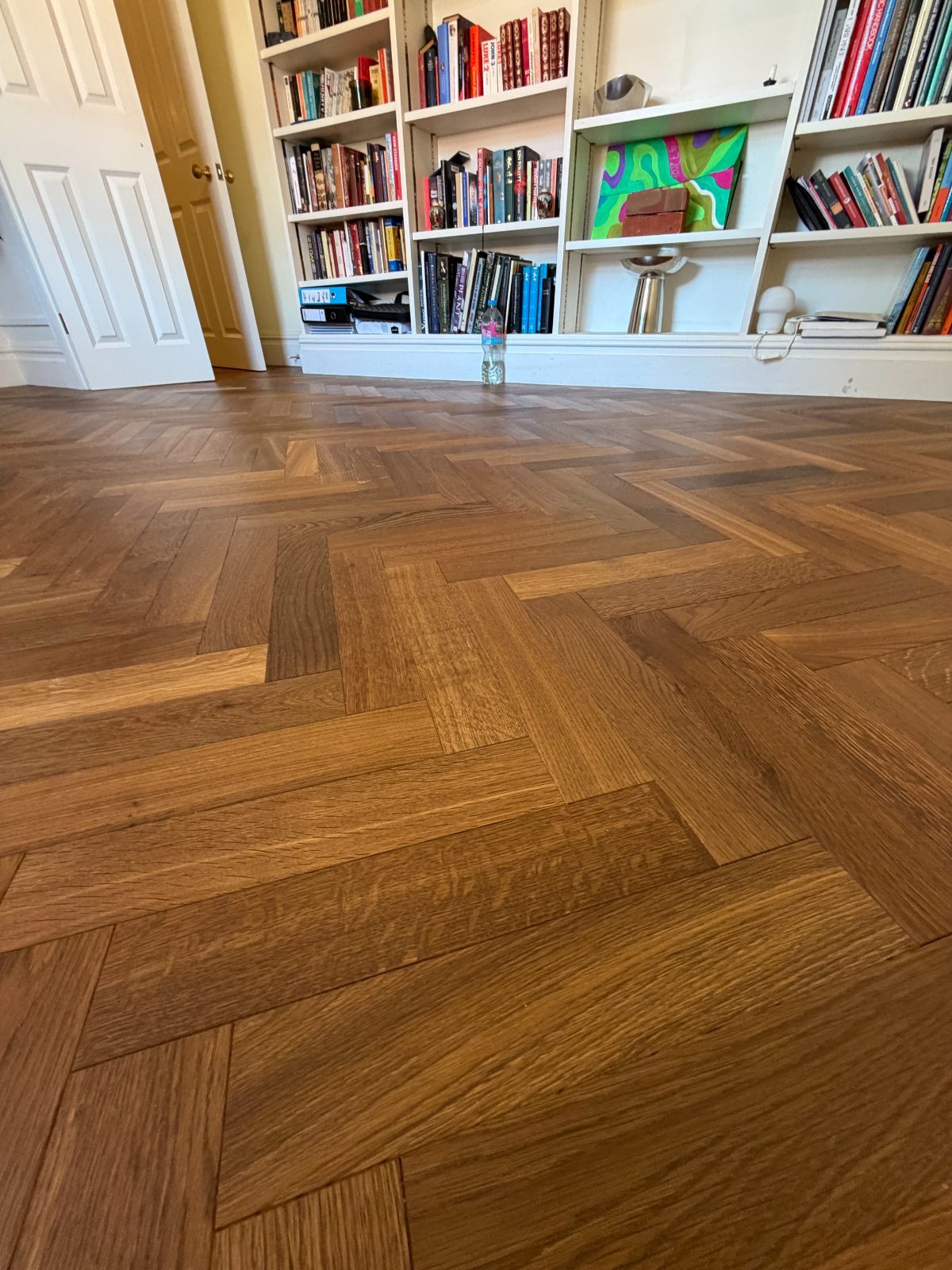 Finished oak herringbone parquet floor running to built-in bookcases and panelled doors in a Burton House library