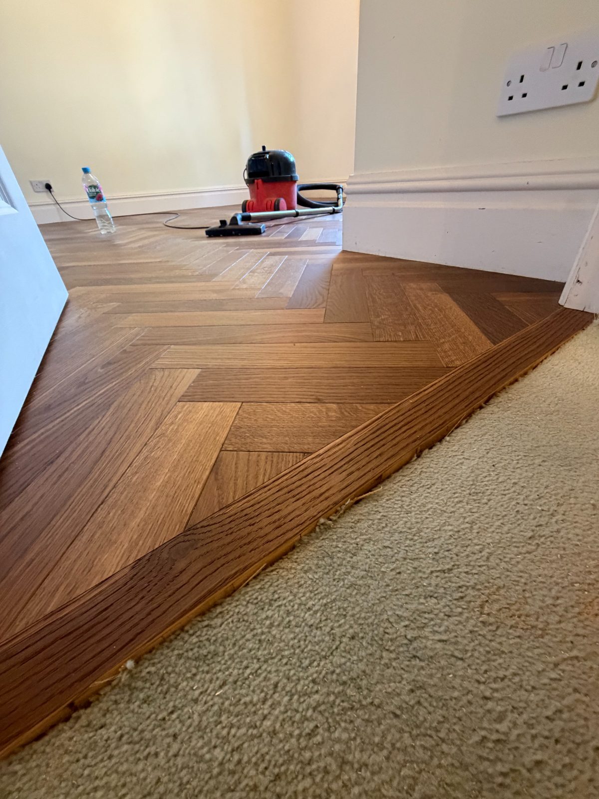 Oak herringbone parquet finished with a plank border where it meets carpet at a doorway in Burton House